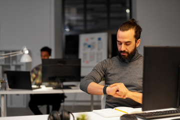 deadline, technology and people concept - creative man with smartwatch and computer working late at night office