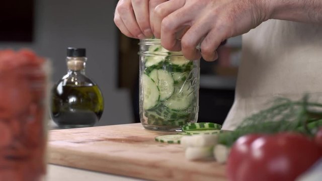 Tracking shot of chef stuffing fresh sliced cucumber into mason jar