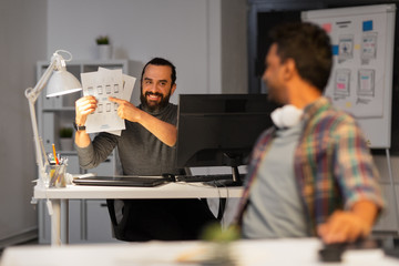 business, deadline and web design people concept - happy creative man showing papers to colleague at night office