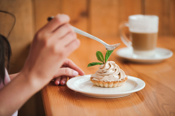 Woman eating a cake of cottage cheese in a ceramic plate with a spoon on a wooden table