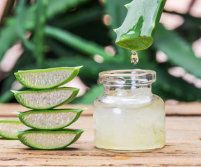 Fresh aloe leaves and aloe gel in the cosmetic jar on wooden table.