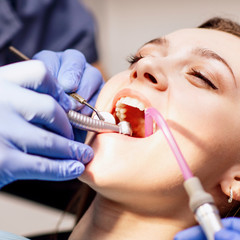Male dentist treating teeth to young woman patient in clinic.