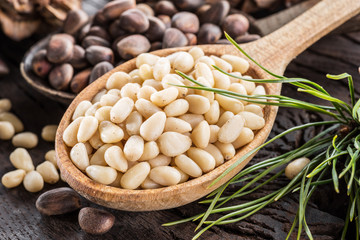 Pine nuts in the spoon and pine nut cone on the wooden table. Organic food.