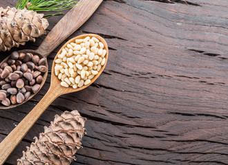 Pine nuts in the spoon and pine nut cone on the wooden table. Organic food.