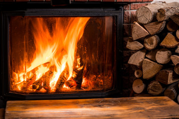 Old wooden table and fireplace with warm fire at the background.