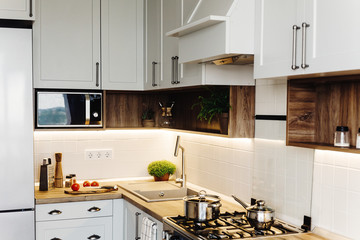 Modern Kitchen design in scandinavian style. stylish light grey kitchen interior with modern furniture and stainless steel appliances. wooden countertop, steel stove, board,knife and spices