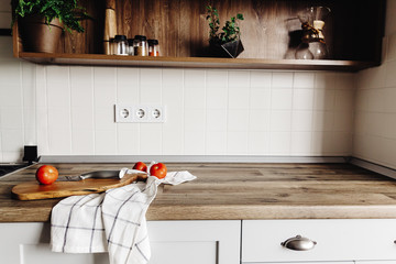 wooden board with knife, tomatoes on modern kitchen countertop and shelf with spices and plants....