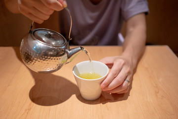 Hand pouring hot japanese green tea from silver metal teapot