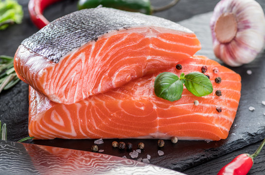 Fresh salmon fillets on black cutting board with herbs and spices.