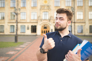 Portrait of a handsome student standing with books in the hands of the university building...