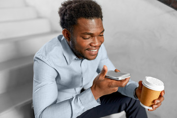 business, communication and technology concept - african american businessman calling or using voice recorder on smartphone at coffee break on office stairs