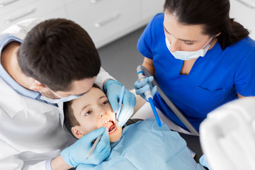 medicine, dentistry and healthcare concept - dentist with mouth mirror and probe checking for kid patient teeth at dental clinic