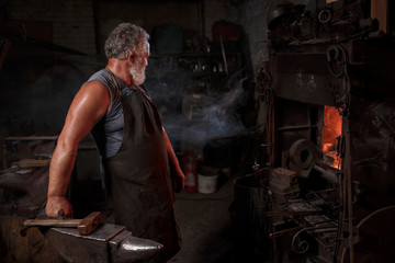 Portrait of a blacksmith artisan in an apron with an anvil in a blacksmith