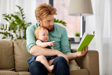 family, fatherhood and people concept - red haired father reading book for little baby daughter at home