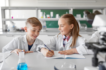 Fototapeta premium education, science and children concept - kids studying chemistry at school laboratory and writing to workbooks
