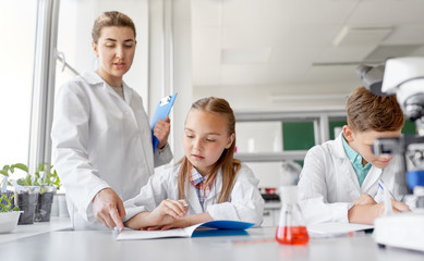Fototapeta premium education, science and children concept - teacher and students studying chemistry at school laboratory and writing to workbooks