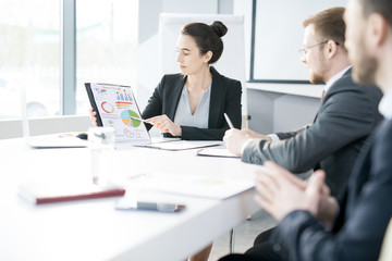 Portrait of beautiful young businesswoman heading meeting sitting at table in conference room and pointing at chart copy space
