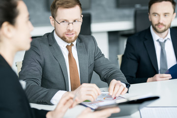 Portrait of successful young businessman talking to colleagues while sitting at meeting table in conference room, copy space