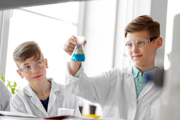 education, science and children concept - boys in goggles with test tube studying chemistry at school laboratory