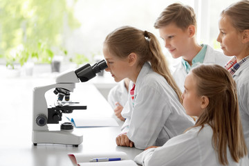 education, science and children concept - kids or students with microscope studying biology at...