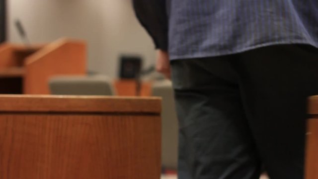 Man walks through the wooden swinging partition in a courtroom.