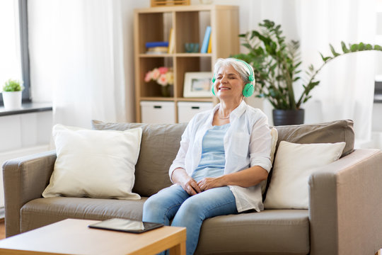 Technology, People And Lifestyle Concept - Happy Senior Woman In Headphones And Tablet Pc Computer Listening To Music At Home