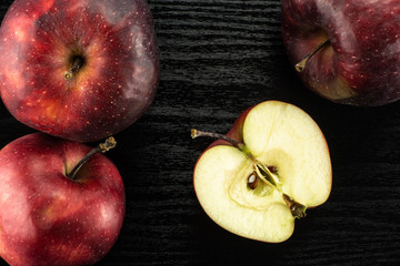 Red delicious three apples and one half flatlay on black wood background.