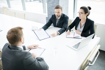 Portrait of three successful business people, man and woman,  talking to partner sitting across meeting table in conference room, copy space