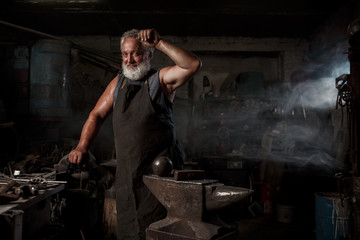 Portrait of a brutal blacksmith artisan in an apron in a blacksmith