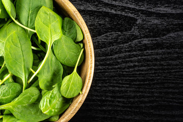 Fresh baby spinach leaves in a wooden bowl top view on black wood background.