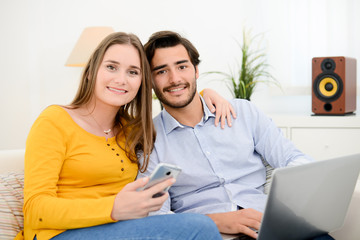 cheerful young couple on sofa at home websurfing and shopping online with laptop computer internet technology