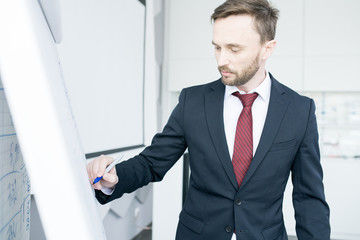 Waist up portrait of handsome businessman writing on whiteboard and explaining marketing strategy  during meeting in conference room