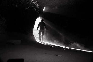 entrance to the cave, a male traveler stands in the rays of light at the exit of the cave,...