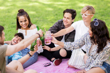leisure, people and celebration concept - happy friends clinking non alcoholic drinks at picnic in summer park