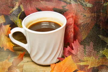 A single hot cup of coffee encircled by leaves in autumn colors on a wooden surface with a texture applied to the fringes of the image.
