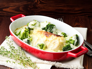 Chicken fillet baked with broccoli in bechamel sauce on dark wooden table. Healthy food, clean eating, side view.