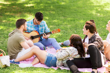 Fototapeta premium friendship, leisure and summer concept - group of happy smiling friends with guitar and non alcoholic beer chilling on picnic blanket at summer park