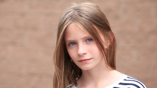 Beautiful blond young girl with freckles outdoors on wall background, close up portrait