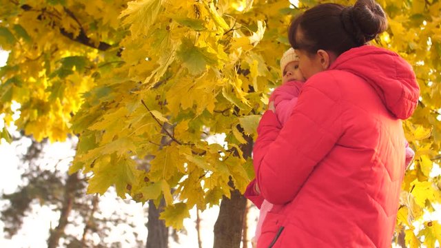 Baby with her mother is looking at autumn leaves and kissing with her mother.