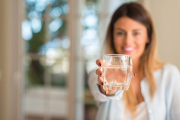 Beautiful young woman smiling while holding a glass of water at home. Lifestyle concept.