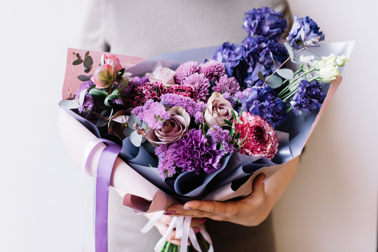 Fototapeta Very nice young woman holding beautiful fresh blossoming bouquet in purple colours of roses, ranunculus, carnations, eustoma, eucalyptus on the grey background