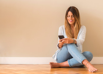 Young beautiful woman smiling sitting on the floor and looking at the phone.