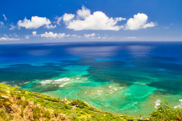 Looking down on the shoreline of Hawaii on a bright, sunny day with lots of blue ocean and reefs.