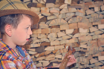 Obraz premium The boy plays the guitar and takes the chords to the dombra, in the background the wood in the village.