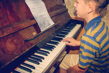 The boy studies chords on notes, sitting at the piano.