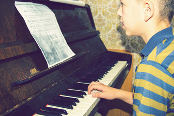 The boy studies chords on notes, sitting at the piano.