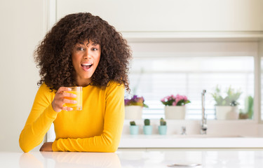 African american woman drinking orange juice in a glass scared in shock with a surprise face, afraid and excited with fear expression
