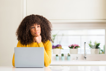 African american woman using computer laptop at kitchen serious face thinking about question, very...