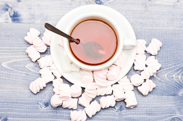 Tea cup with dipped teabag and marshmallows. Process of drink brewing in mug, top view. Mug filled with black brewed tea, spoon and heap of marshmallow on wooden background. Tea break concept