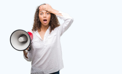Young hispanic woman holding megaphone stressed with hand on head, shocked with shame and surprise face, angry and frustrated. Fear and upset for mistake.